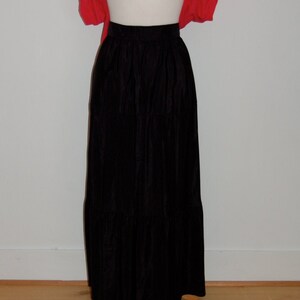 May include: A black maxi skirt with multiple tiers. The skirt is worn with a bright pink cropped cardigan.