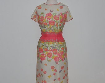 Könnte beinhalten: Ein Vintage-Kleid mit Blumenmuster mit rosa, gelben und grünen Blumen auf weißem Hintergrund. Das Kleid hat einen rosa Gürtel und kurze Ärmel.