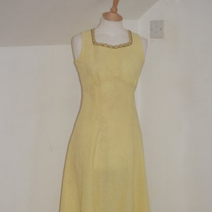 May include: A sleeveless maxi dress in a pale yellow color with a gold trim around the neckline.