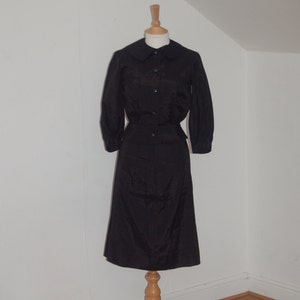 May include: A black skirt suit with a collared blouse and long sleeves. The skirt is knee-length and the blouse has a button-up front.
