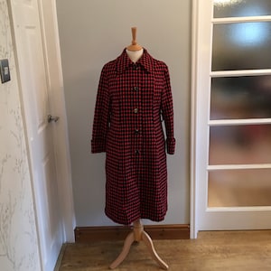 May include: A long red and black checkered coat with a button closure. The coat has a collar and long sleeves.