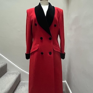May include: A long, double-breasted red coat with a black velvet collar and cuffs. The coat features black buttons and a tailored fit, displayed on a mannequin. A classic, elegant outerwear piece.