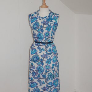 Pode incluir: Um vestido branco sem mangas com estampa floral azul e roxo. O vestido tem um cinto preto e está em um manequim de madeira.