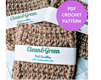 Może przedstawiać: Dwa brązowe, szydełkowe gąbki do mycia naczyń wykonane z juty, z białą etykietą z napisem "Clean & Green Dish Scrubbies (100% biodegradable Jute)". Różowe koło z tekstem "PDF CROCHET PATTERN" znajduje się w prawym górnym rogu obrazu.