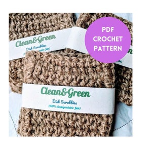 以下が含まれることがあります： ジュート製の茶色のクロシェ編み食器洗いスポンジが2つ。白いラベルには「Clean & Green Dish Scrubbies (100% biodegradable Jute)」と書いてあります。画像の右上には、「PDF CROCHET PATTERN」と書かれたピンク色の円があります。