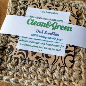 Może przedstawiać: Dwa brązowe gąbki do mycia naczyń z juty z etykietą z napisem "Clean & Green Dish Scrubbies (100% biodegradable Jute)" i instrukcjami dotyczącymi czyszczenia gąbek.