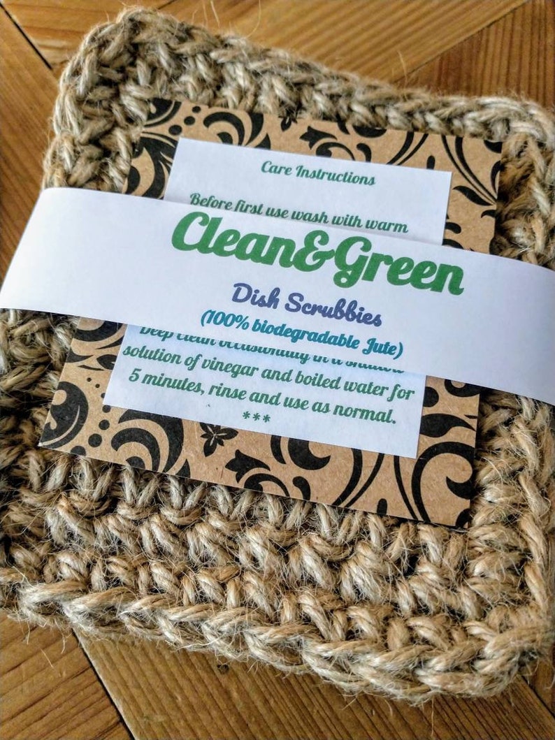 Może przedstawiać: Dwa brązowe gąbki do mycia naczyń z juty z etykietą z napisem "Clean & Green Dish Scrubbies (100% biodegradable Jute)" i instrukcjami dotyczącymi czyszczenia gąbek.