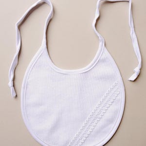 May include: White baby bib with a lace trim and adjustable straps.