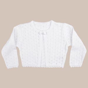 May include: White knitted baby cardigan with a bow detail at the neckline. The cardigan has a scalloped edge and long sleeves.