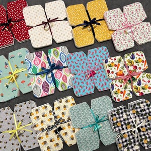 May include: A collection of 10 fabric gift boxes, each with a different pattern. The boxes are folded flat and tied with ribbon. The patterns include bees, watermelons, leaves, flowers, and checkered patterns.