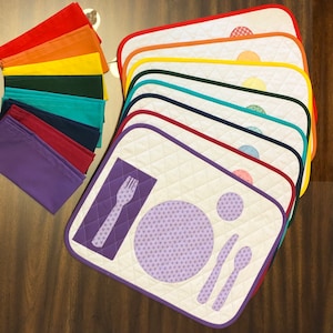May include: A set of 10 placemats in various colors, each with a white center featuring a quilted design and a purple fork, knife, and plate. The placemats are lined with a contrasting color trim.
