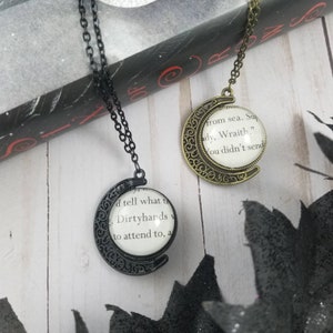 Puede incluir: Dos collares con colgantes circulares que contienen texto de una página de libro bajo una cúpula de cristal. Un colgante tiene un marco y cadena de metal negro, el otro tiene un marco y cadena de bronce antiguo. El texto es visible.