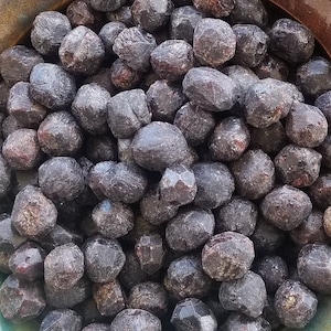 May include: A bowl filled with dark red, almost black, round gemstones. The bowl is a mottled brown and green ceramic with a glossy finish. The bowl is being held by a hand.