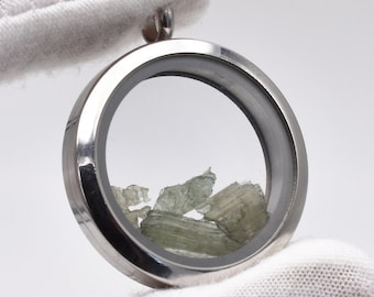 May include: A silver locket pendant with a clear glass insert containing small green crystals.
