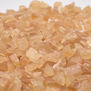 May include: A close-up of a pile of light brown, translucent, irregularly shaped sugar crystals. A ruler is visible in the bottom right corner of the image.