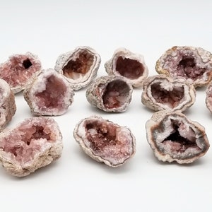 May include: A collection of pink amethyst crystal geodes, each with a unique shape and size. The geodes are arranged on a white surface, showcasing their natural beauty.