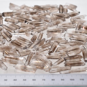 Peut inclure: Un ensemble de pointes de cristal de quartz fum&eacute; brut. Les cristaux, de couleur gris-brun&acirc;tre translucide, varient en taille et en forme. Une r&egrave;gle gradu&eacute;e en centim&egrave;tres est visible au bas de l'image.
