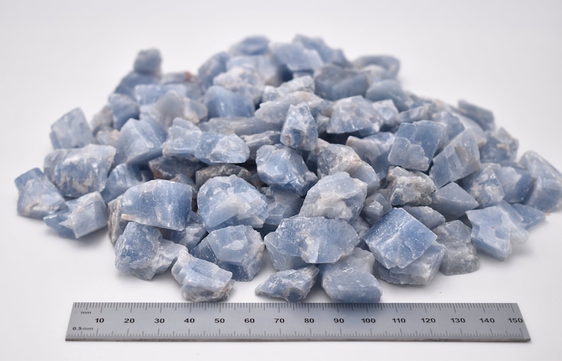 May include: A pile of light blue celestite crystal chips, measuring approximately 1.5 inches in diameter, against a white background. A ruler is placed below the pile of crystals for scale.