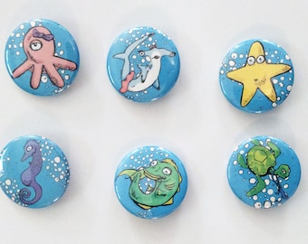 May include: Six colorful buttons with different sea creatures on a blue background. The creatures include an octopus, a hammerhead shark, a starfish, a seahorse, a fish, and a sea turtle.