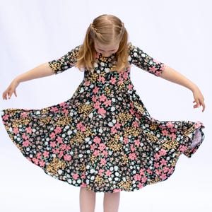May include: A black floral print dress with pink and yellow flowers. The dress has three-quarter sleeves and a flared skirt. The model is wearing the dress and has their arms outstretched, showing off the skirt.