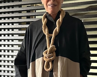 May include: A woman with short, grey hair wearing black sunglasses and a black and beige tunic with a thick, knotted rope necklace.