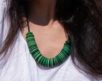 May include: A woman wearing a white shirt with a green and black layered necklace and matching earrings.