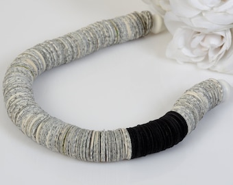 May include: A necklace made of paper circles, with a black band at the end. The circles are white with black print.