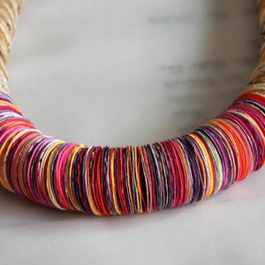 May include: A colorful necklace made of stacked paper circles in shades of red, orange, yellow, white, purple, and pink.