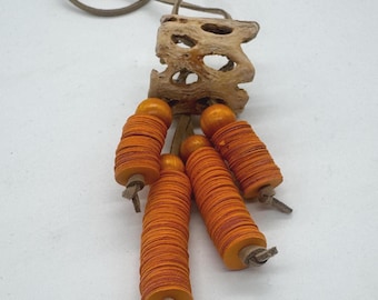 May include: A handcrafted necklace with a natural wood pendant and a series of orange, stacked disc beads. The necklace has a leather cord. The beads are cylindrical and have a textured appearance. The background is neutral.