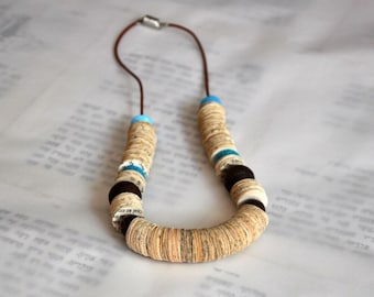 May include: A unique necklace made from rolled paper beads in beige and brown tones, interspersed with blue and black beads. It is strung on a brown cord and has a magnetic clasp.