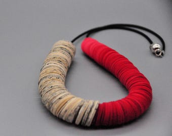 May include: A distinctive necklace with a two-tone design. One half is beige, made of stacked circular pieces, and the other is red with a layered texture. The necklace is strung on a black cord with a silver clasp.