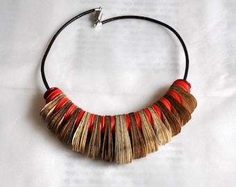 May include: A distinctive necklace with a black leather cord and a central pendant crafted from layered book pages and red details. The pendant is about 15 cm wide, offering a bold, eye-catching design.