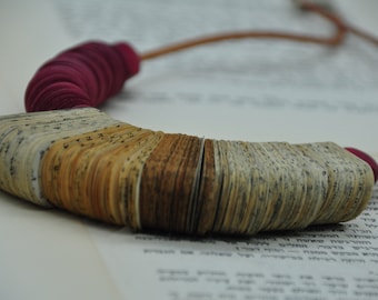 May include: A necklace made from stacked pages of a book, with a burgundy fabric accent. The pages are layered to create a unique and textured design.