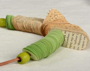 Peut inclure: Un collier original composé de pages de livre et de perles de papier vertes. Le collier a un cordon en cuir et des perles en bois. Les pages du livre sont pliées en forme d'éventail, et les perles de papier vertes sont empilées.
