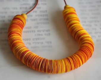 May include: A necklace made of stacked, round, paper discs in shades of yellow and orange. The necklace is strung on a brown cord.