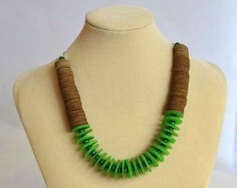 May include: A distinctive necklace displayed on a mannequin. The necklace combines brown and green elements. The upper section is made of stacked brown discs, and the lower section features green, circular components. A striking piece of jewellery.
