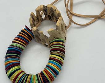 May include: A distinctive necklace with a natural wood pendant and a vibrant, circular beaded design. The beads are in various colours, including red, blue, yellow, and green, strung together. The necklace has a brown leather cord. The necklace is a unique piece of jewellery.
