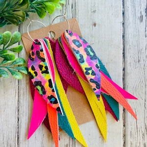 May include: A pair of dangle earrings with a hoop design. The earrings feature multiple layers of leather in various colors, including pink, orange, yellow, green, and a leopard print.