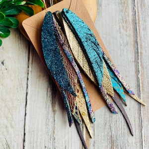 May include: Teal, gold, and brown leather earrings with a glitter finish. The earrings are shaped like leaves and are hanging from gold hoops.