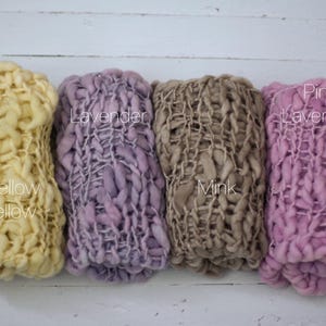 May include: Four chunky knit scarves in a row, each a different color. From left to right, the colors are mellow yellow, lavender, mink, and pink lavender. Each scarf has a unique texture and the name of the color is written on the scarf.