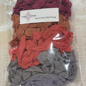 May include: A clear plastic bag filled with fabric strips in shades of burgundy, brown, coral, and gray. The bag has a white label with the text "Triple V Vintage" and a website address.