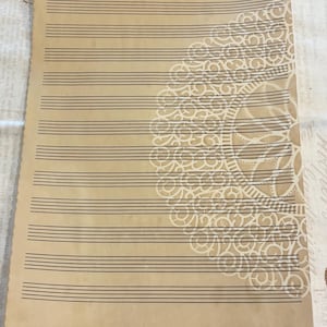 May include: A sheet of tan-colored music manuscript paper featuring twelve black horizontal staves. The right side of the paper displays a large, intricate white circular mandala pattern. The text HL00210045 is printed at the top center.