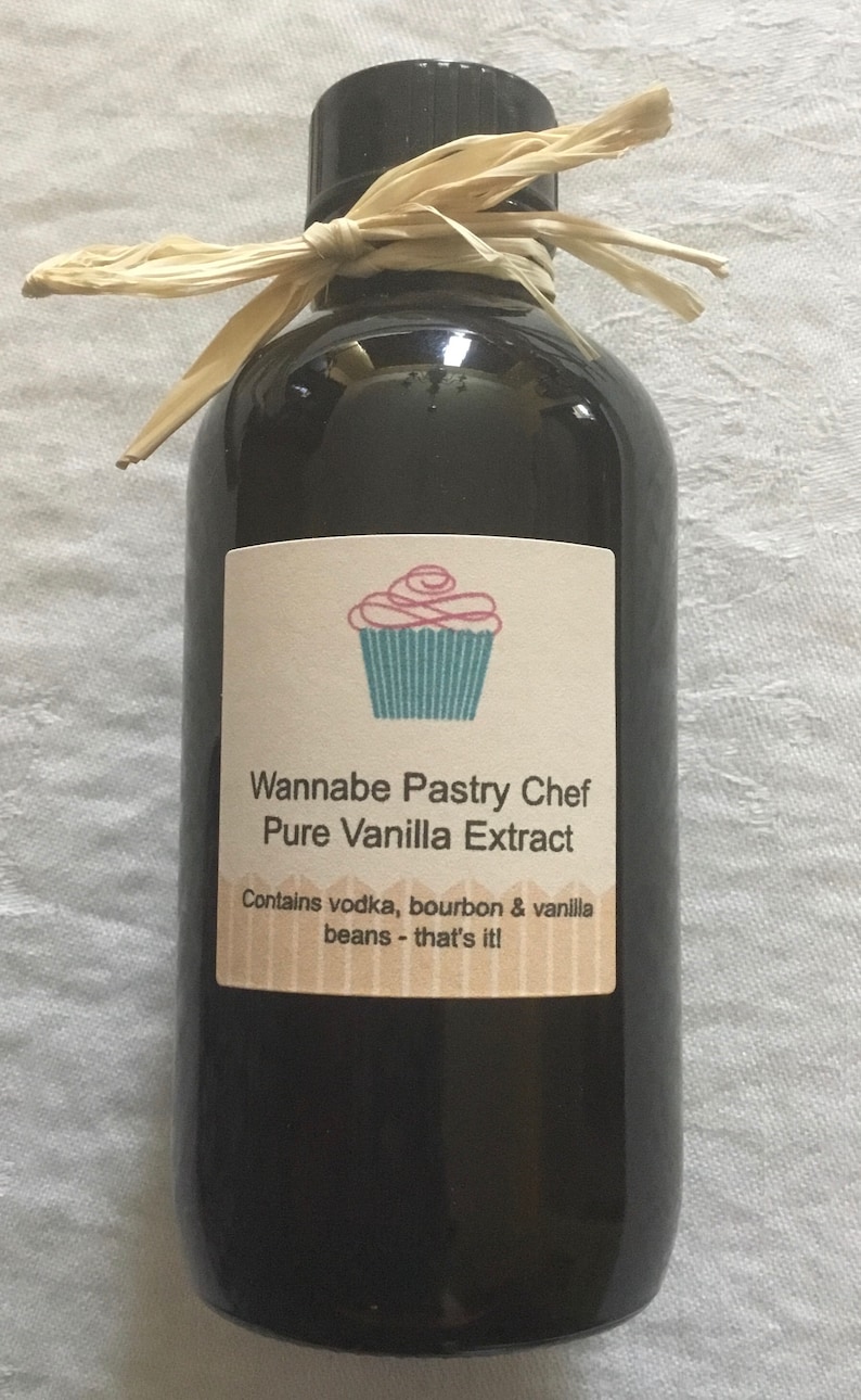 May include: A glass bottle of pure vanilla extract with a brown label that says "Wannabe Pastry Chef Pure Vanilla Extract" and "Contains vodka, bourbon & vanilla beans - that's it!" The bottle is tied with a brown raffia ribbon.
