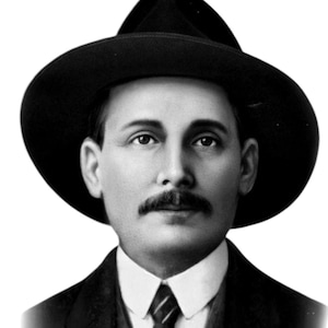 May include: A monochrome portrait of a man in a wide-brimmed hat, dark suit, and tie. The man has a moustache and a serious expression. The image is a vintage photograph.