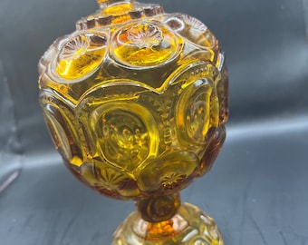 May include: Amber glass candy dish with a round, footed base and a domed lid. The dish is decorated with a repeating pattern of stars and moons.