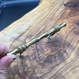 May include: A brass drawer pull with a decorative bamboo design. The pull has two round knobs on each end.