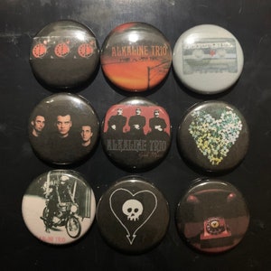 May include: Nine round buttons with different designs featuring the band Alkaline Trio. The buttons feature band photos, album covers, and band logos.