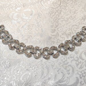 May include: A silver bracelet with a chain of interlocking heart-shaped links, each set with clear rhinestones.