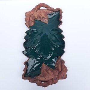 May include: A ceramic serving tray in the shape of a leaf, with a glossy teal interior and a brown, textured exterior. The tray features detailed leaf accents around the edges and a handle at the top, perfect for serving appetizers or decorative display.