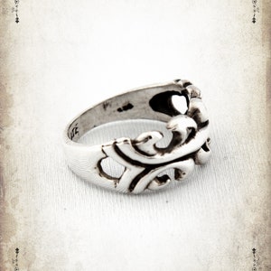 Puede incluir: Un anillo de plata con un dise&ntilde;o detallado y ornamentado. El anillo est&aacute; hecho de una sola pieza de metal y tiene un acabado liso y pulido.